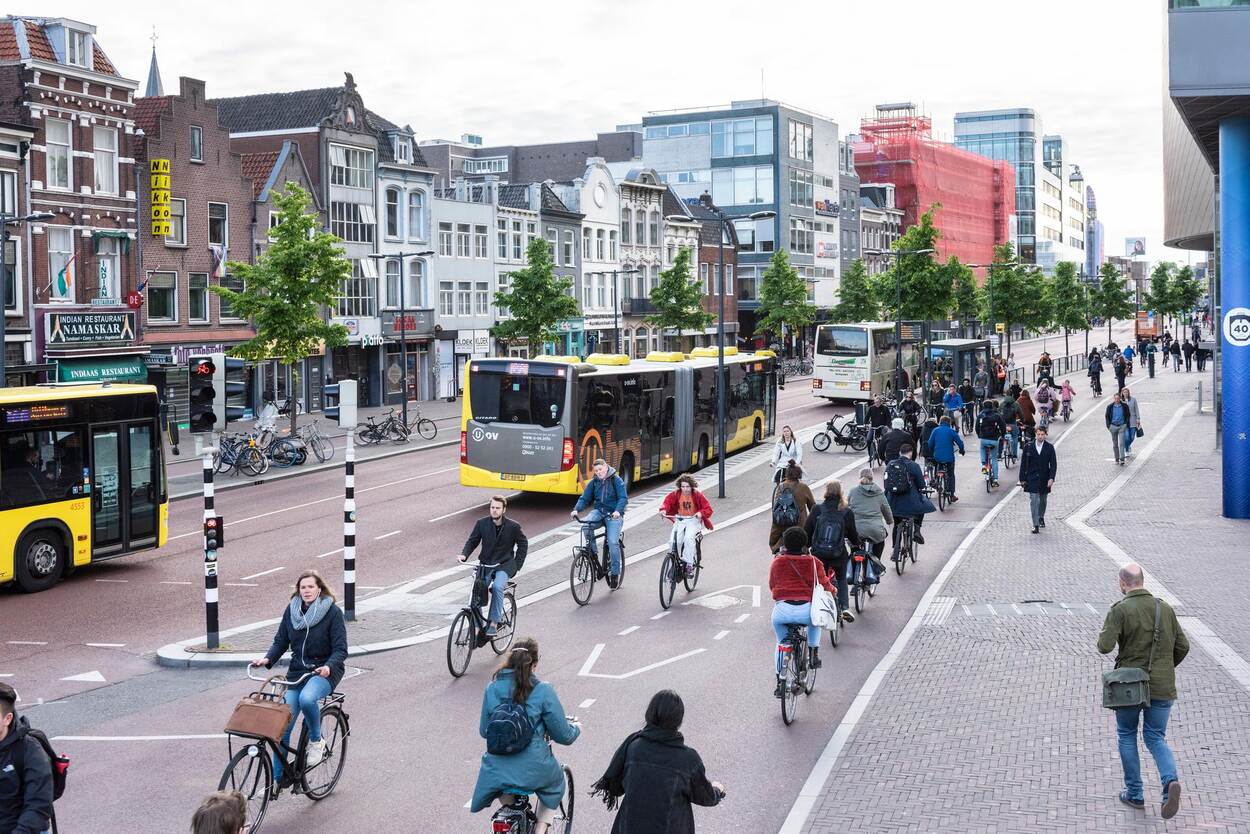 afbeelding met in het midden een fietspad vol fietsers, links een bushalte en rechts een drukke stoep