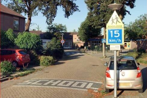 een straat met het woord 'school' in tegels op de grond en een schoolzone bord naast de weg